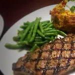 White plate with grilled steak, green beans and a loaded baked potato