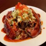 White plate with a BBQ dish, topped with coleslaw and sauce