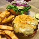 Open burger on a bun with lettuce, pickles, red onion and a side of fries