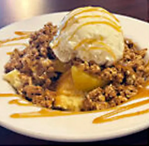 Peach Cobbler Crisp dessert on a plate with vanilla ice cream and caramel drizzle on top 