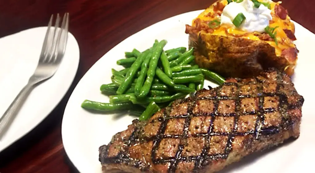 Grilled steak, green beans and a loaded baked potato on a white dinner plate