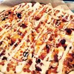 Photo of a pizza with toppings and sauce drizzled on top.