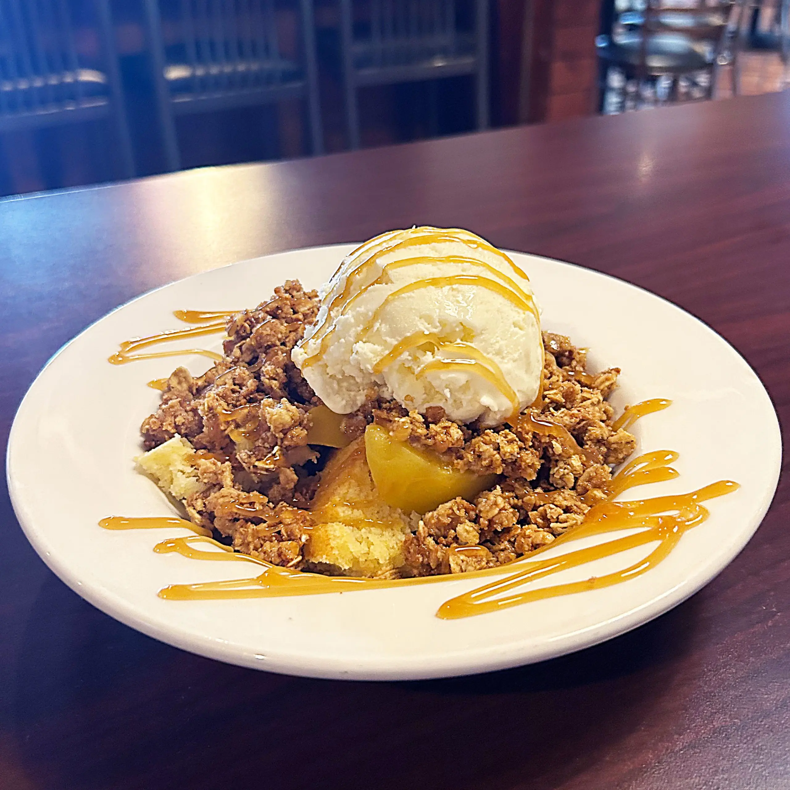 Peach Cobbler Crisp dessert on a plate with vanilla ice cream and caramel drizzle on top 